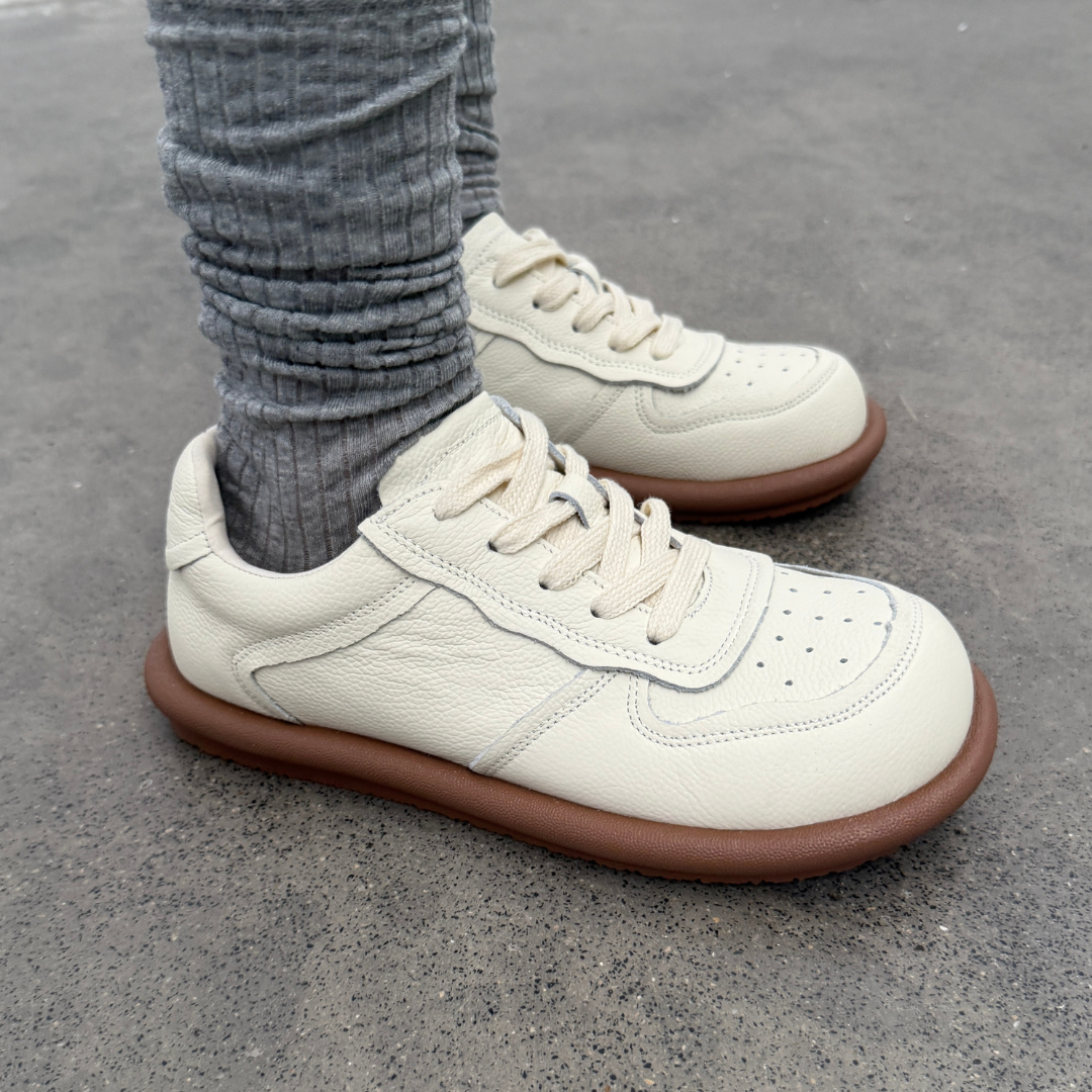 White sneakers with brown soles worn on a concrete surface