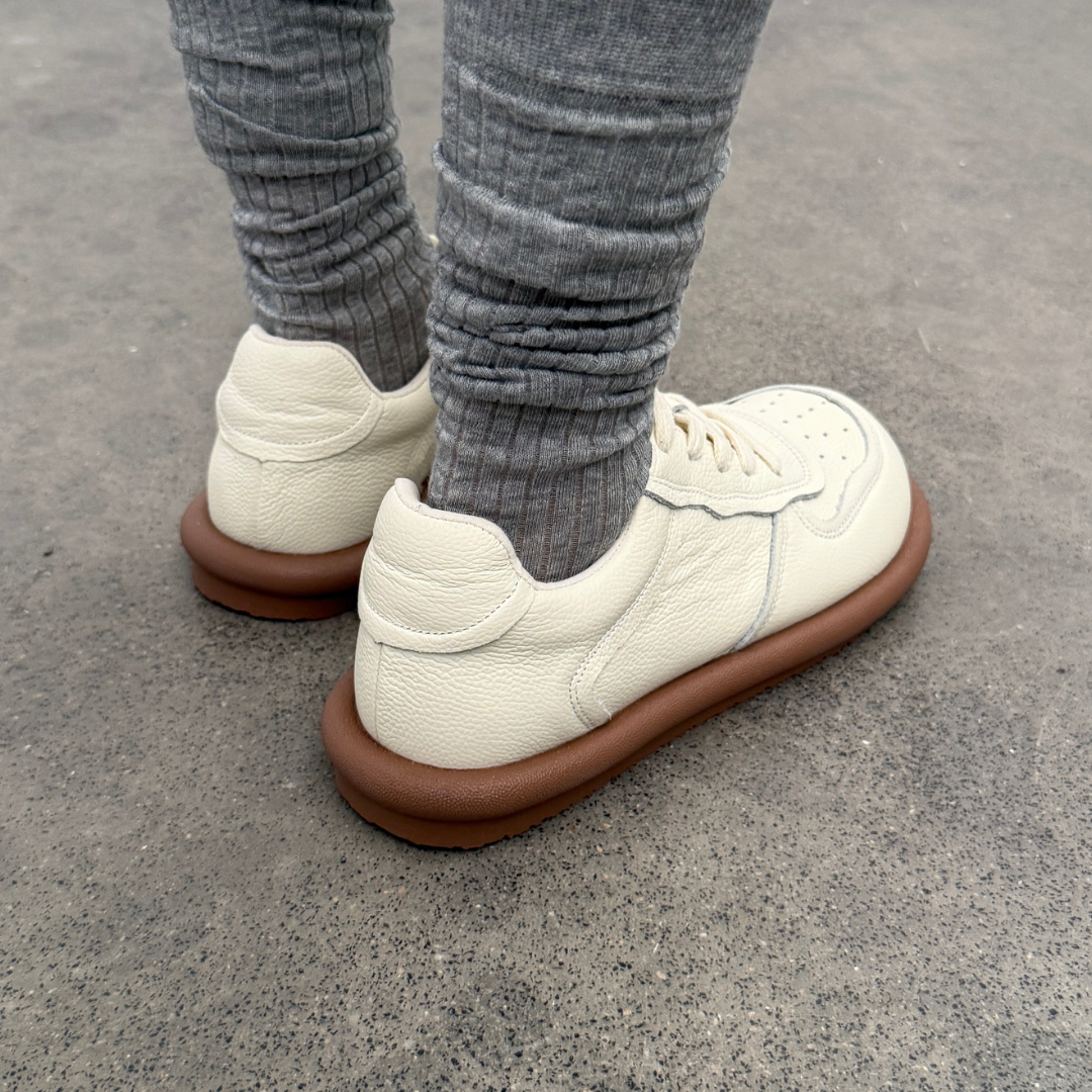 White sneakers with brown soles worn with gray pants on a concrete surface