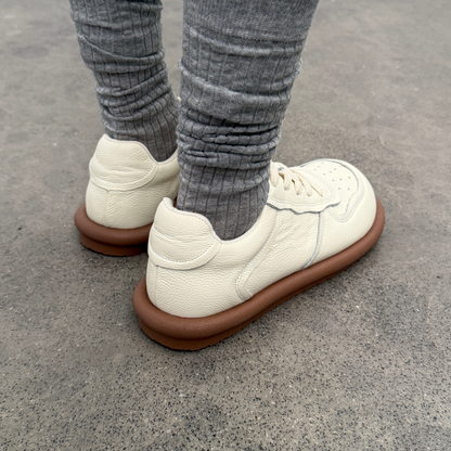 White sneakers with brown soles worn with gray pants on a concrete surface