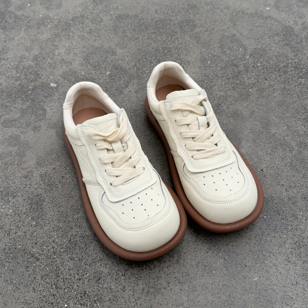 Pair of white sneakers with brown soles on a gray concrete surface