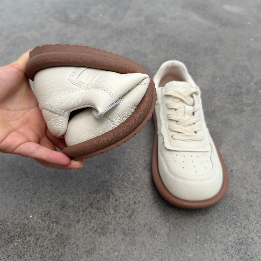 White sneakers with brown soles on a gray pavement