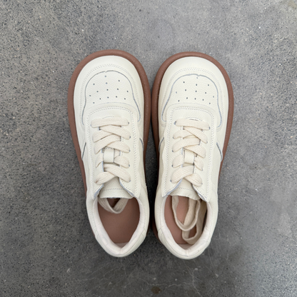 Pair of white sneakers with brown soles on a gray concrete surface