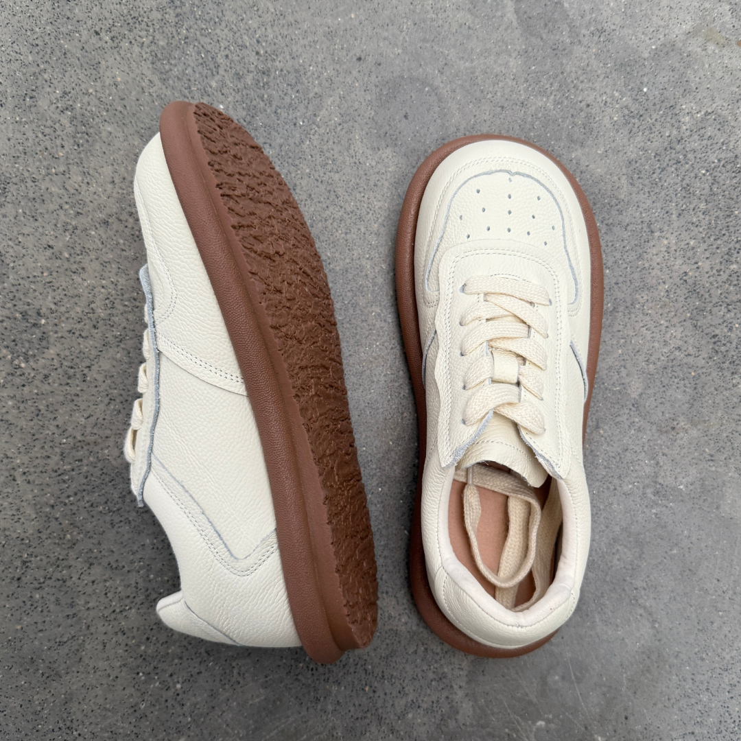 White sneakers with brown soles on a gray concrete surface