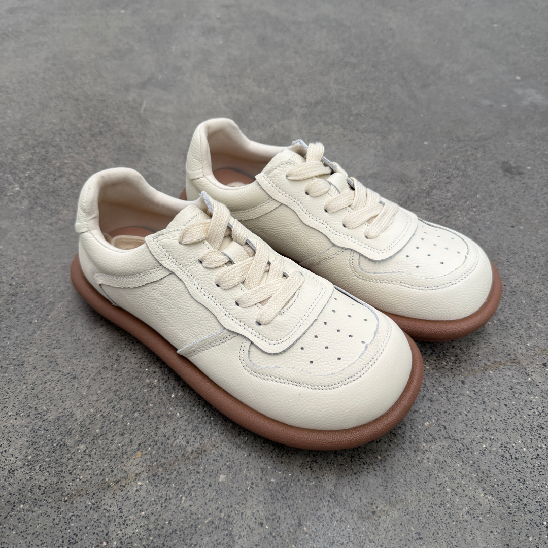 Pair of beige sneakers with brown soles on a gray concrete surface