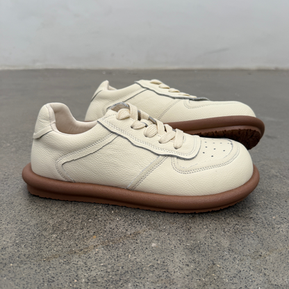 Pair of cream sneakers with brown soles on a gray concrete floor