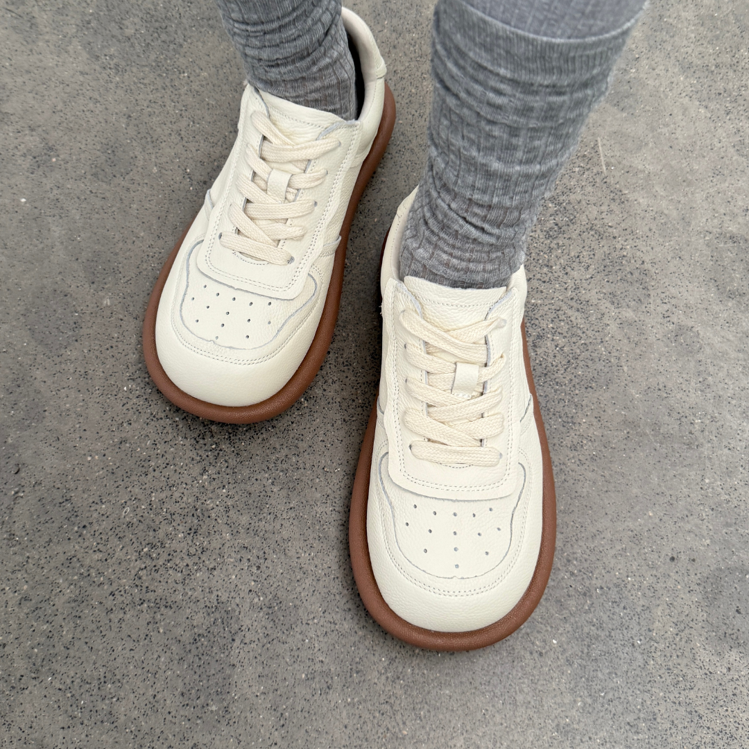 White sneakers with brown soles worn on a concrete surface