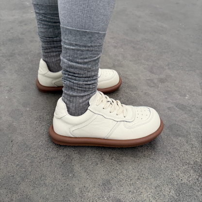 White sneakers with brown soles worn by a person on a concrete surface